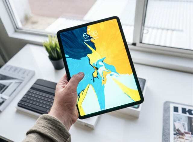 iPad med fargerik tapet holdt over et hvitt skrivebord