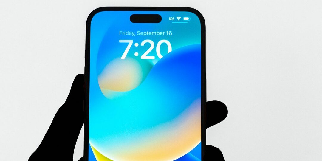 Fotka osoby držící iPhone se staženým iOS 16