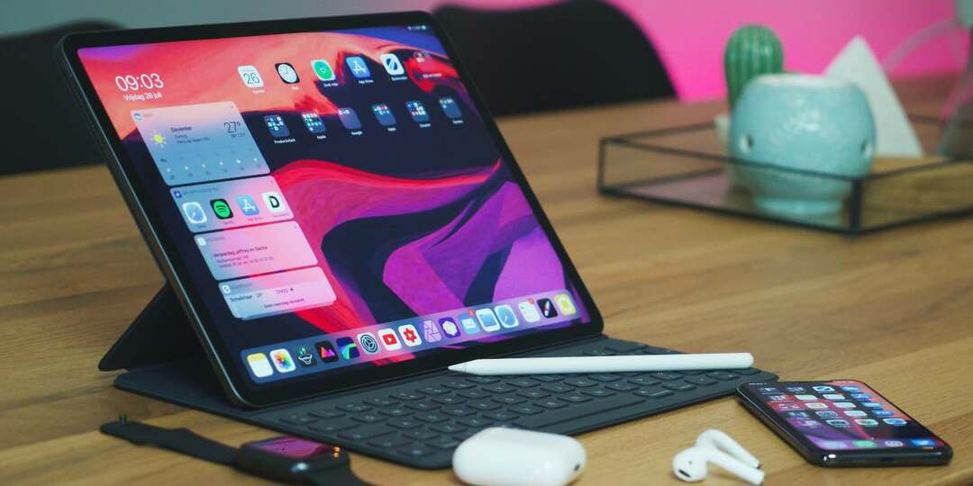 Φωτογραφία ενός iPad σε ένα τραπέζι με Apple Pencil, iPhone και AirPods
